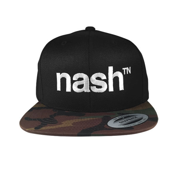 Black baseball cap with white letters on a white background. The hat visor is flat and is brown, black, green and tan camouflage. The white letters are embroidery stitched on the front and say nashᵀᴺ. Nash is short for Nashville and TN is the abbreviation for Tennessee. There is a silver and black oval sticker on the visor that says SNAPBACK.