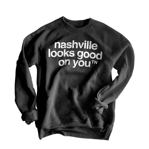 Black crew sweatshirt with white text on white background. The sleeves are rolled and the sweatshirt looks slightly wrinkled. The nashᵀᴺ slogan, nashville looks good on youᵀᴺ is printed in white and centered on shirt.    