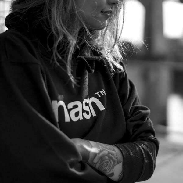 Lady wearing black hooded sweatshirt. Her arms are crossed. Her left arm has a rose tattoo.