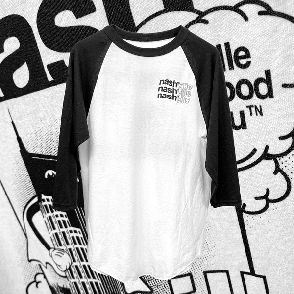 White and black baseball T-shirt on black and white graphic background. nashᵀᴺville is printed three times on the left chest in a wavy style.