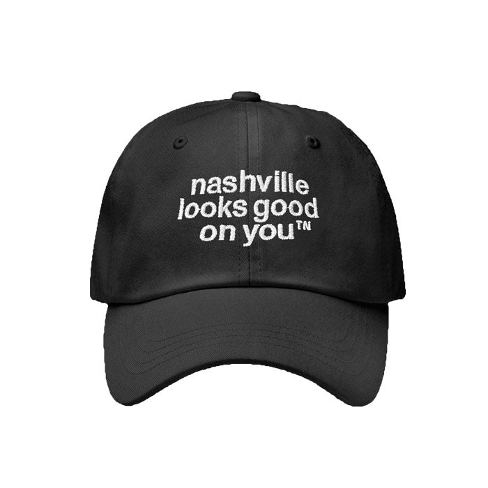 Black baseball cap with white letters on a white background. Hat is angled slightly to the left and has nashville looks good on youᵀᴺ embroidered in black on the front of the cap. The visor is slightly curved and there is a silver and black oval shaped sticker on the visor that says Authentic Classics.
