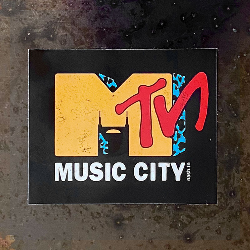 Mᵀᴺ  sticker shown on a textured surface. Nashville is known as Music City. The parody sticker shows the Batman Building in the negative space of the letter M and large letters TN across the right side of the letter M. White, block text reads Music City underneath the letter M. 