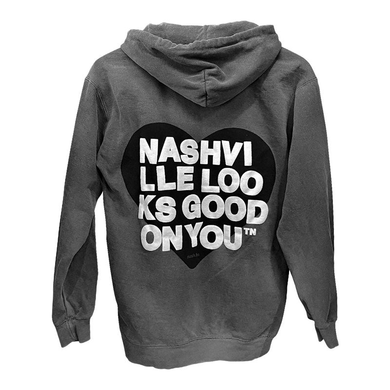 Back side of gray hooded sweatshirt on a white background. Backside has a black heart with white text printed on top that reads nashville looks good on youᵀᴺ in wrapped text. 