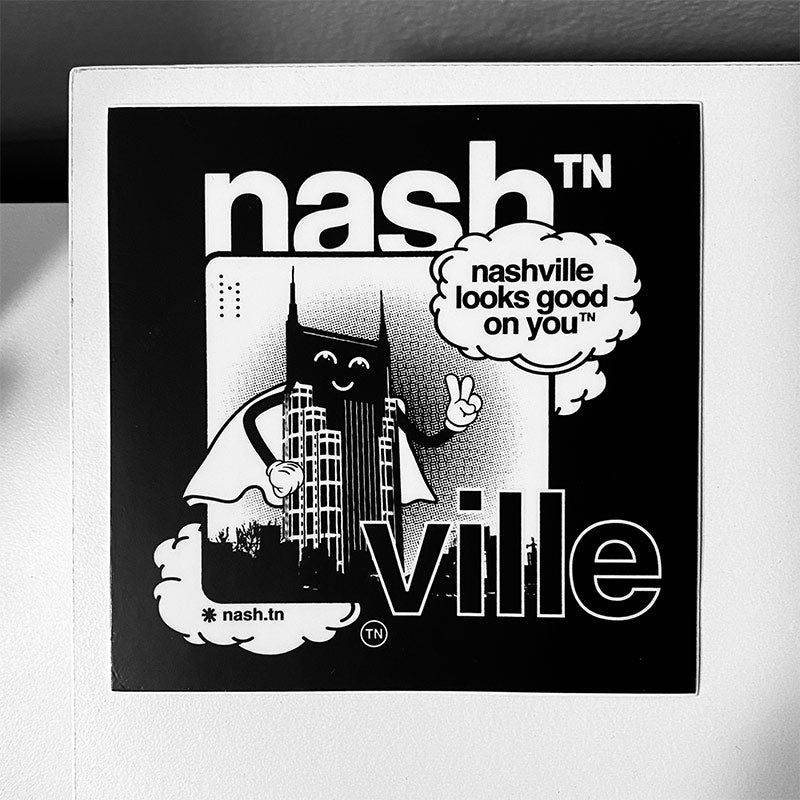 Black square sticker on white background. The nashᵀᴺ ville sticker features, Batty, the nashᵀᴺ  cartoon character showing a peace sign with it's hand. The batty character pays homage to Nashville's Batman Building. 