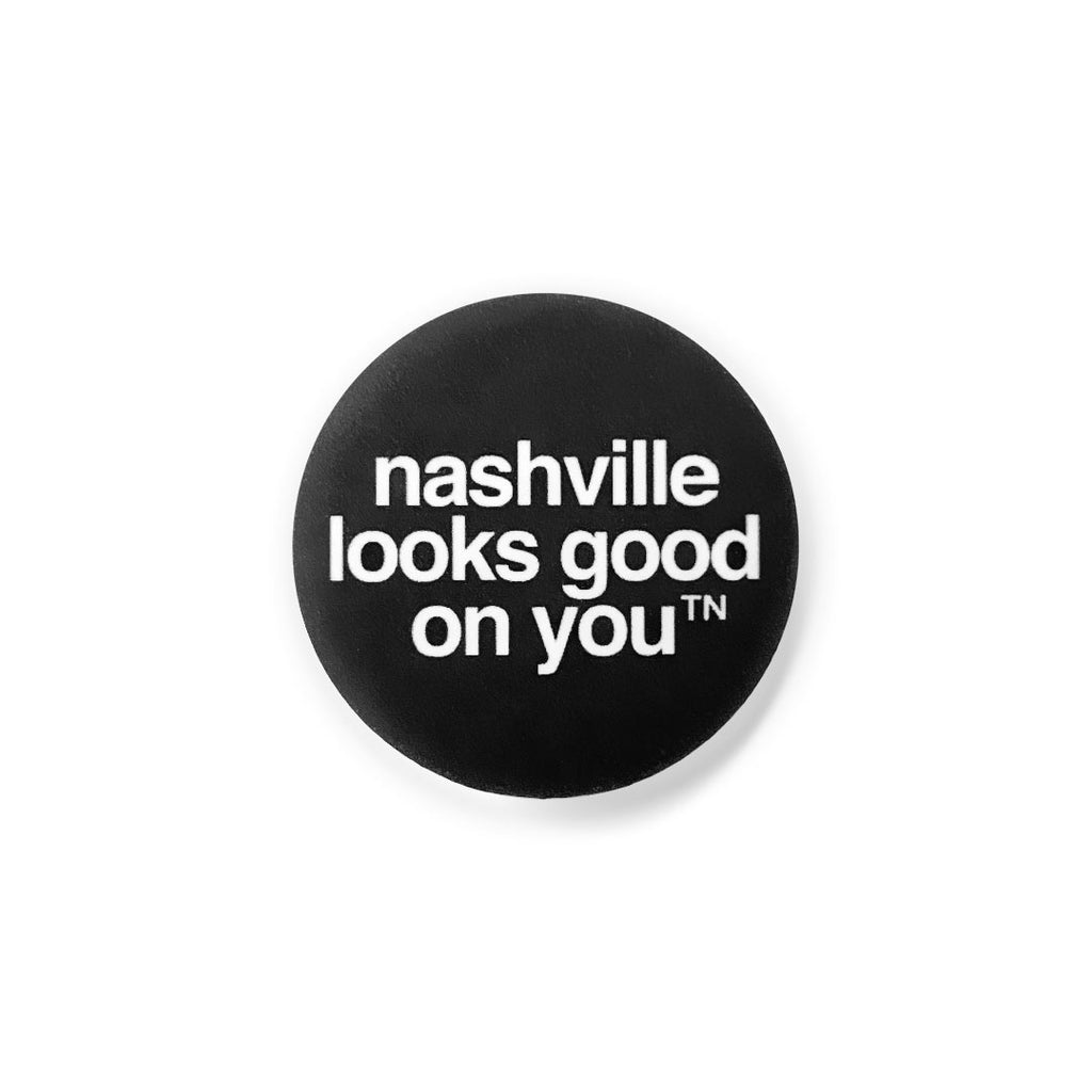 Black round lapel pin button on a white background. The pin has the slogan nashville looks good on youᵀᴺ in white  