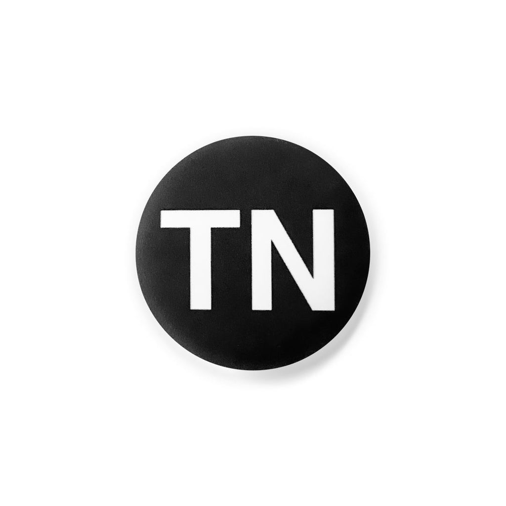 Black, round lapel pin button on a white background. The button has the letters TN in white. TN is the abbreviation for Tennessee.