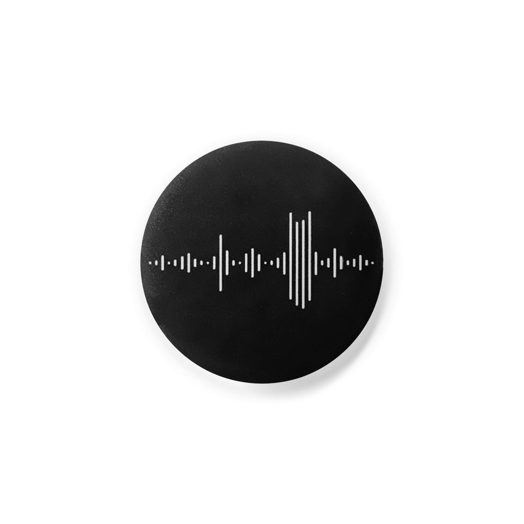 Black, round lapel pin button on a white background. The button has white vertical lines that represents both a wav audio file and the Nashville skyline. The Batman building is prominent in the skyline.The use of a wav file symbol is important because Nashville is known as Music City.