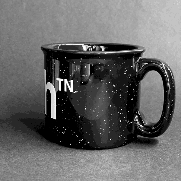 Spinning video of black campfire mug on a gray background. The black mug has white speckles and white text that reads nashᵀᴺ  across the front.