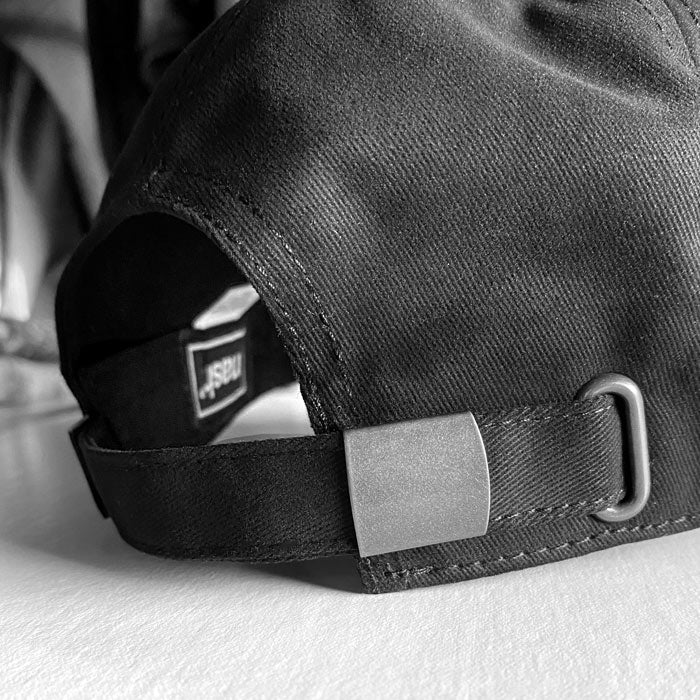 Close up detail of the black baseball cap's adjustable sizing metal buckle.