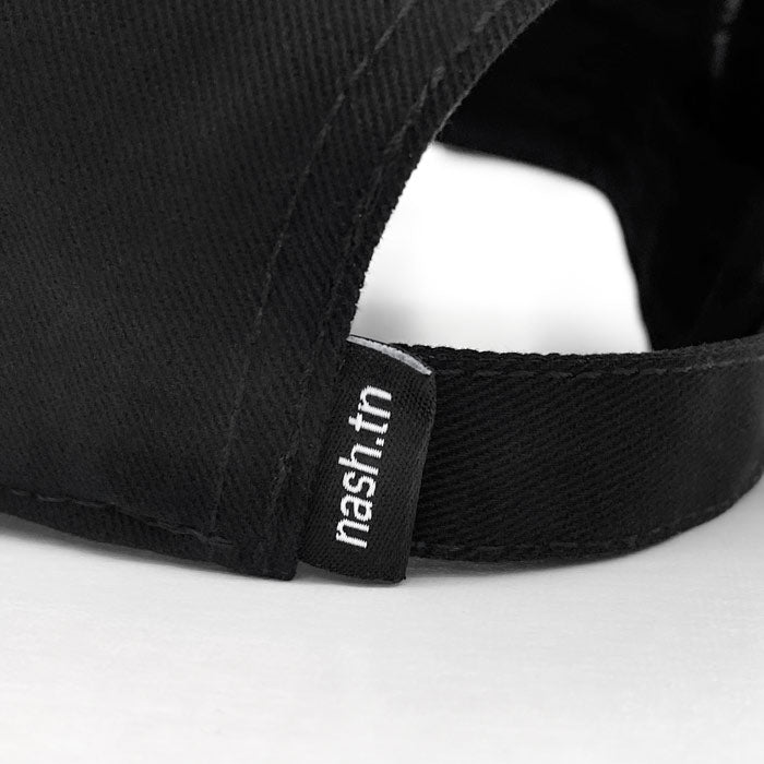Close up detail of the black baseball cap on a white background. There is a small, black label tag with nash.tn in white  at the sizing band.