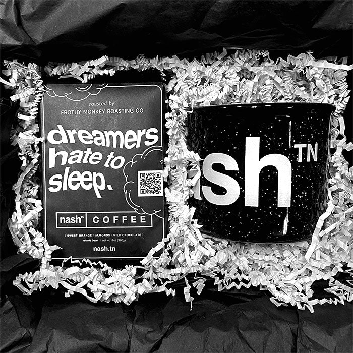 Two items shown on top of white crinkle paper box filler. Black coffee bag on the left with white, wavy text on the front that reads, "dreamers hate to sleep." On the right, there is a black coffee mug with white speckles and partial white, letter logo showing. White letters s, h. There is a superscript TN next to the letter h. TN is the abbreviation of Tennessee.