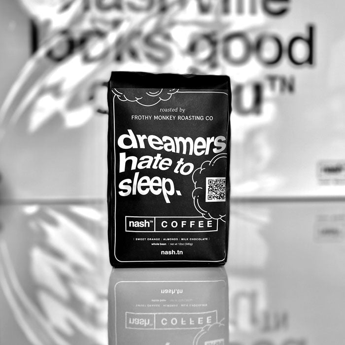 Black coffee bag with a label that has white text and cloud shape outlines. The text is wavy and says dreamers hate to sleep. The photo background is white with black blurry text that says nashville looks good on you TN.