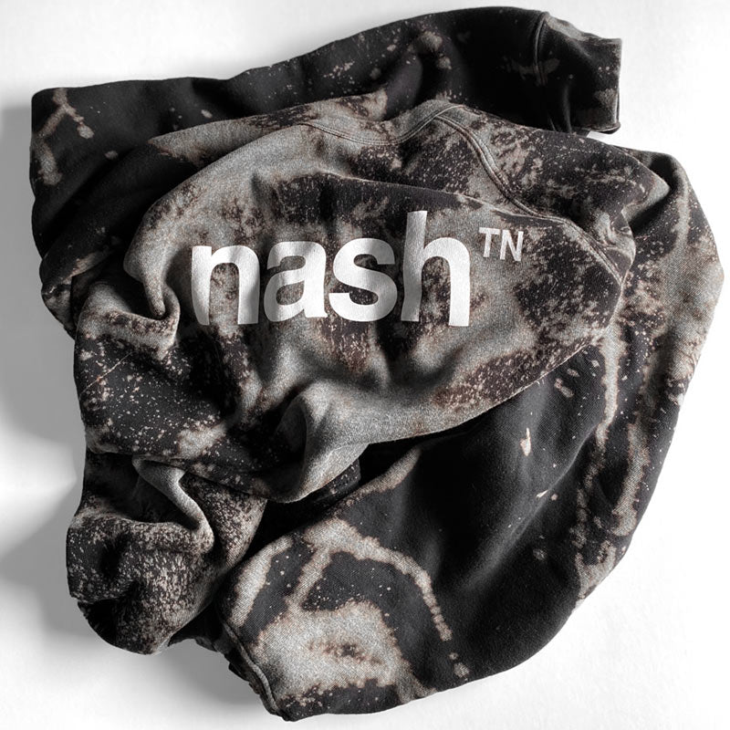 Crew sweatshirt shown folded and crumpled on a white background. The nashᵀᴺ  logo is printed in white on the front of the sweatshirt. The sweatshirt has been dyed and bleached to have to have a marbled appearance with grays, browns and blues. The patterns are random with streaks, spots and splatters.