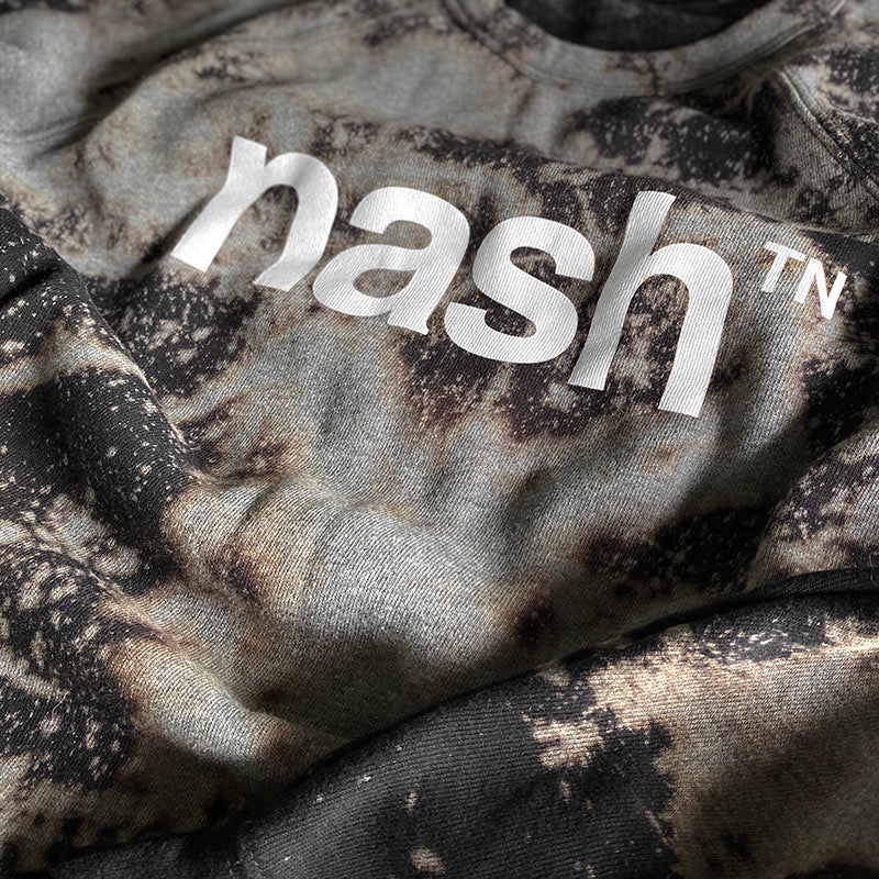 Closeup look of the bleach and dye patterns and nashᵀᴺ  logo printed in white. The sweatshirt has been dyed and bleached to have to have a marbled appearance with grays, browns and blues