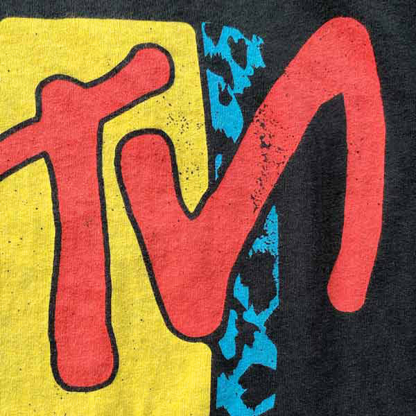 Closeup look at the vintage- style printing of a parody design. The letters TN are in red across a yellow block with a blue cheetah print accent block.