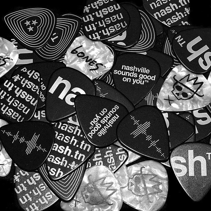 A mixture of Nashville- themed guitar picks on a table. Some picks are white with black designs and others are black picks with white designs. 