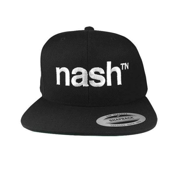 Black baseball cap with white letters on a white background. The hat visor is flat. The white letters are embroidery stitched on the front and say nashᵀᴺ. Nash is short for Nashville and TN is the abbreviation for Tennessee. There is a silver and black oval sticker on the visor that says SNAPBACK.