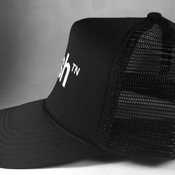 Side view of black trucker baseball hat on light gray background. The visor is pointed to the left.