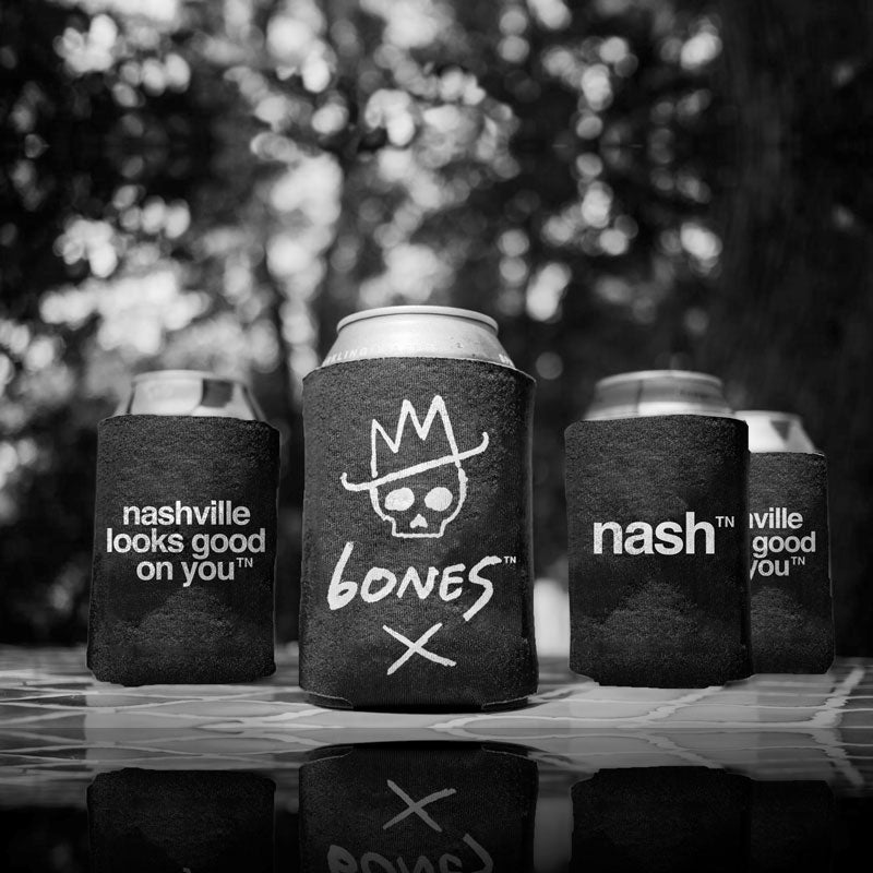 Metal drink cans in black koozies arranged in a v-pattern to show the various designs. Can one in the rear on the left: black koozie with white letters nashville looks good on youᵀᴺ  Can two center front: skull with white cowboy hat and X  with white letters 6ONE5 can three rear right: black koozie with white letters nashᵀᴺ  Can four far rear right: black koozie with white letters nashville looks good on youᵀᴺ 