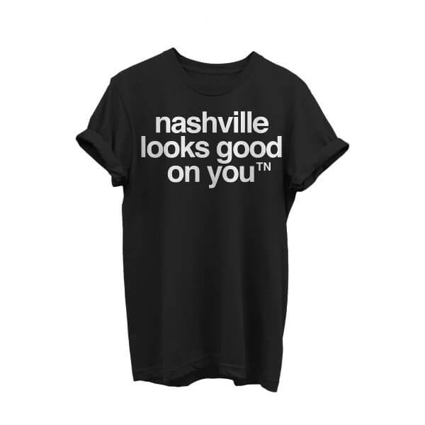 Black crewneck short sleeve T-shirt with white text on white background. The sleeves are rolled. The nashᵀᴺ slogan, nashville looks good on youᵀᴺ is printed in white and centered on shirt.