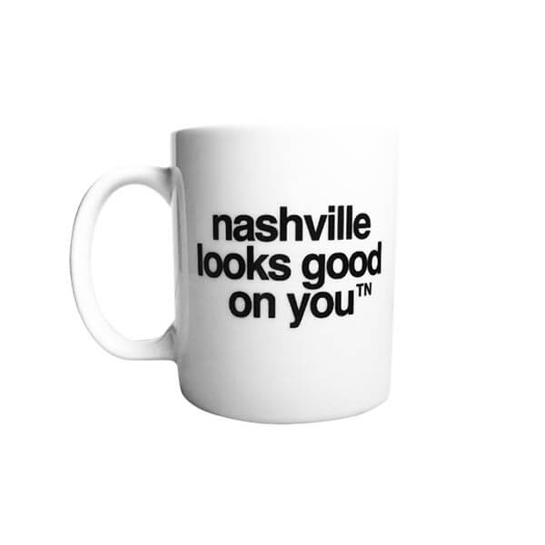 White coffee mug with black text on a white background. nashville looks good on youᵀᴺ is printed in black in the center of the mug.  