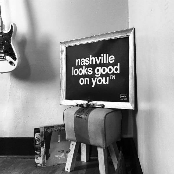A framed black rectangle is propped up in a corner.  The frame contained a poster of the nashᵀᴺ  slogan,  nashville looks good on youᵀᴺ printed in white.