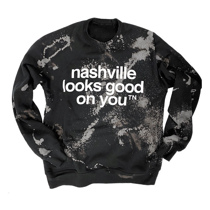 Black crew sweatshirt on white background. The sweatshirt has the nashᵀᴺ slogan nashville looks good on you nashᵀᴺ printed in white. The sweatshirt has been dyed and bleached to have to have a marbled appearance with grays, browns and blues.