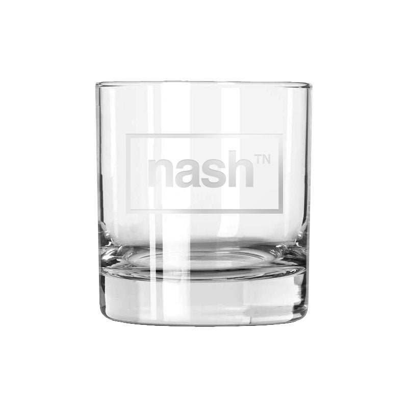 Clear rocks glass with frosted letters on a white background. On the front center of the glass, nashᵀᴺ inside of a horizontal rectangle is etched