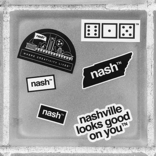 Six stickers removed from the sticker sheet and placed randomly on a gray metal square. The six stickers are: nashville looks good on youᵀᴺ, where creativity livesᵀᴺ, a TN shaped sticker, nashᵀᴺ in white text, nashᵀᴺ in black text and 615 dice
