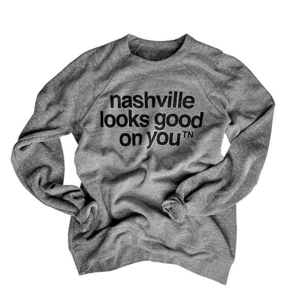 Gray crewneck sweatshirt with black letters on a white background. The cuffs are rolled up and the shirt appears wrinkled. Nashville looks good on youᵀᴺ is printed on the front of the sweatshirt in black.  