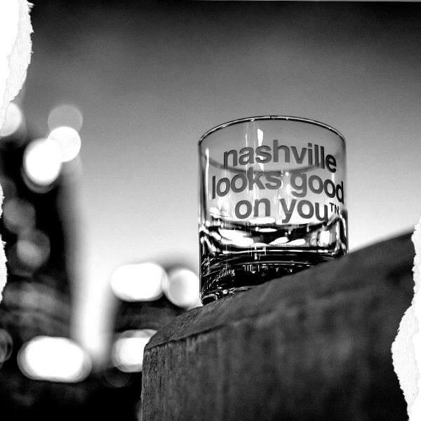 Clear glass with frosted letters on a blurry background. On the front center of the glass, nashᵀᴺ slogan nashville looks good on youᵀᴺ is etched.