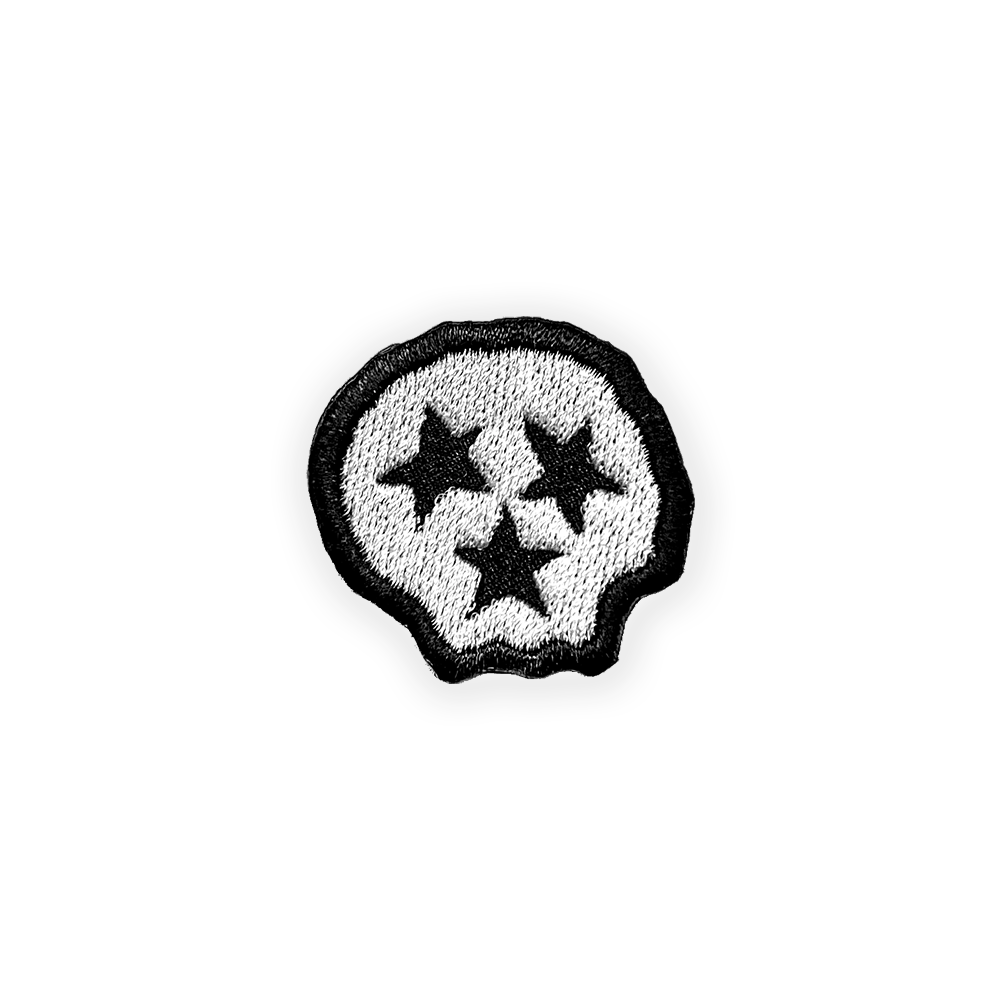 A close up look at the white skull shaped patch. The skull is outlined in black and there are three black stars that represent both the face of the skull and the three grand division of Tennessee: East, Middle, West. Tennessee is known as the Tri-star state.