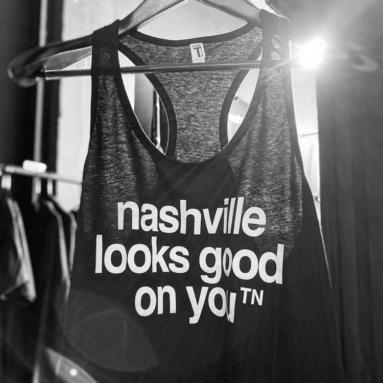 Black tank top with white letters hang on a hanger with bright sun shining at the top.