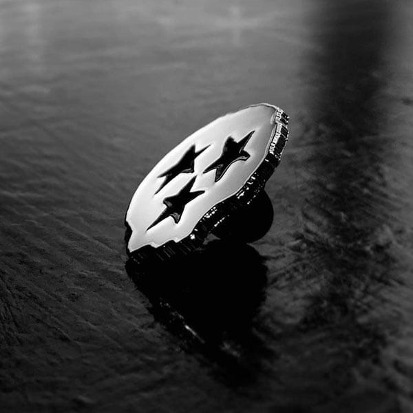 Side view of a white, skull-shaped, fashion pin showing the thickness of the enamel pin.