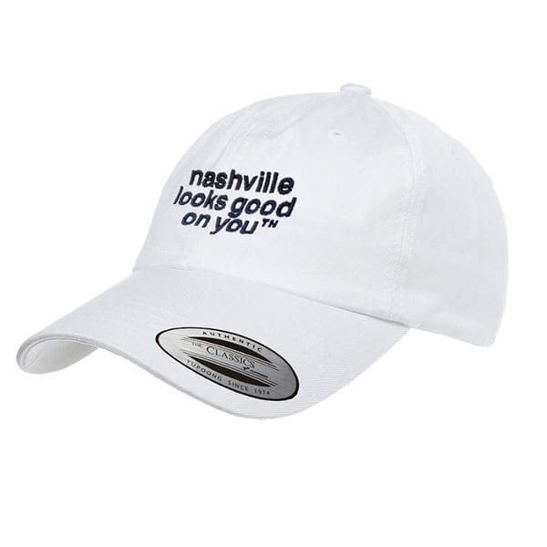 White baseball cap with black letters on a white background. Hat is angled slightly to the left and has nashville looks good on youᵀᴺ embroidered in black on the front of the cap. The visor is slightly curved and there is a silver and black oval shaped sticker on the visor that says Authentic Classics.