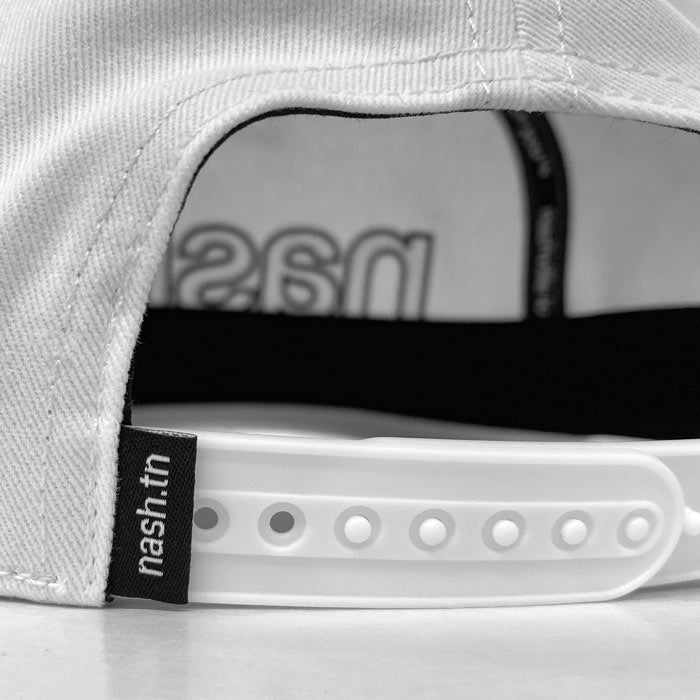 Back side view of white baseball cap on a white background. There is a black tag with white letters to the left of a white adjustable sizing snap. The tag reads nash.tn in white letters.